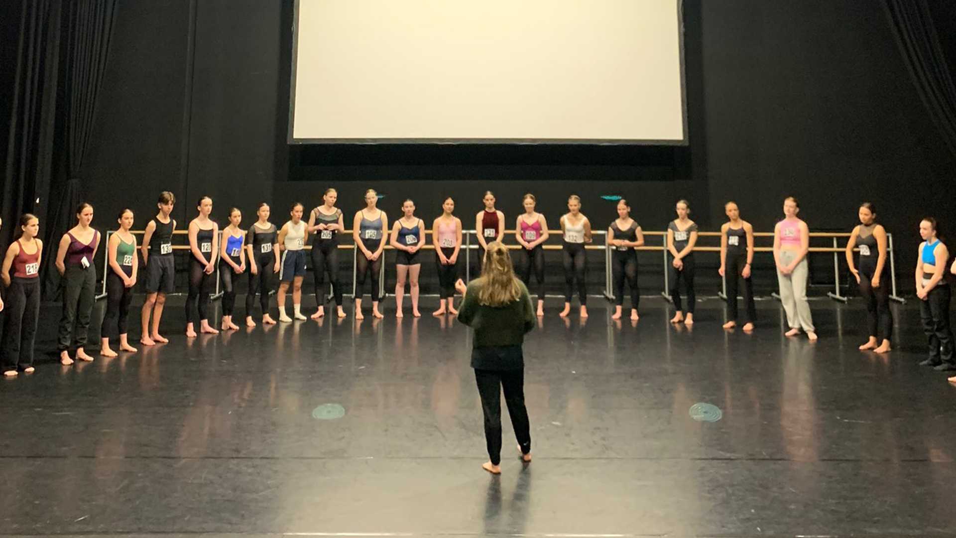 Dansers in een lange rij van links naar rechts met repetitor ervoor